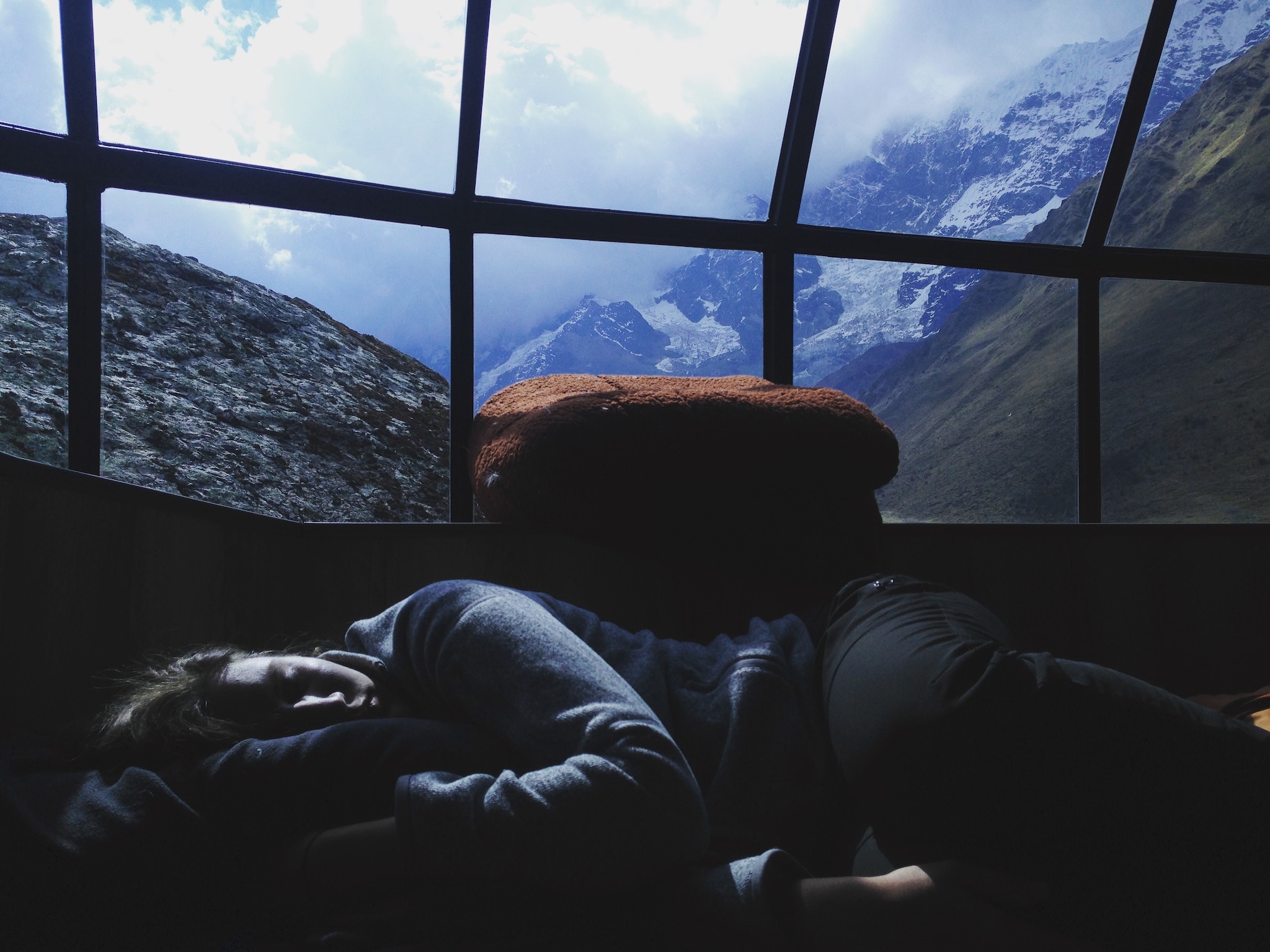 traveler sleeping under large windows in the mountains, likely jet lagged