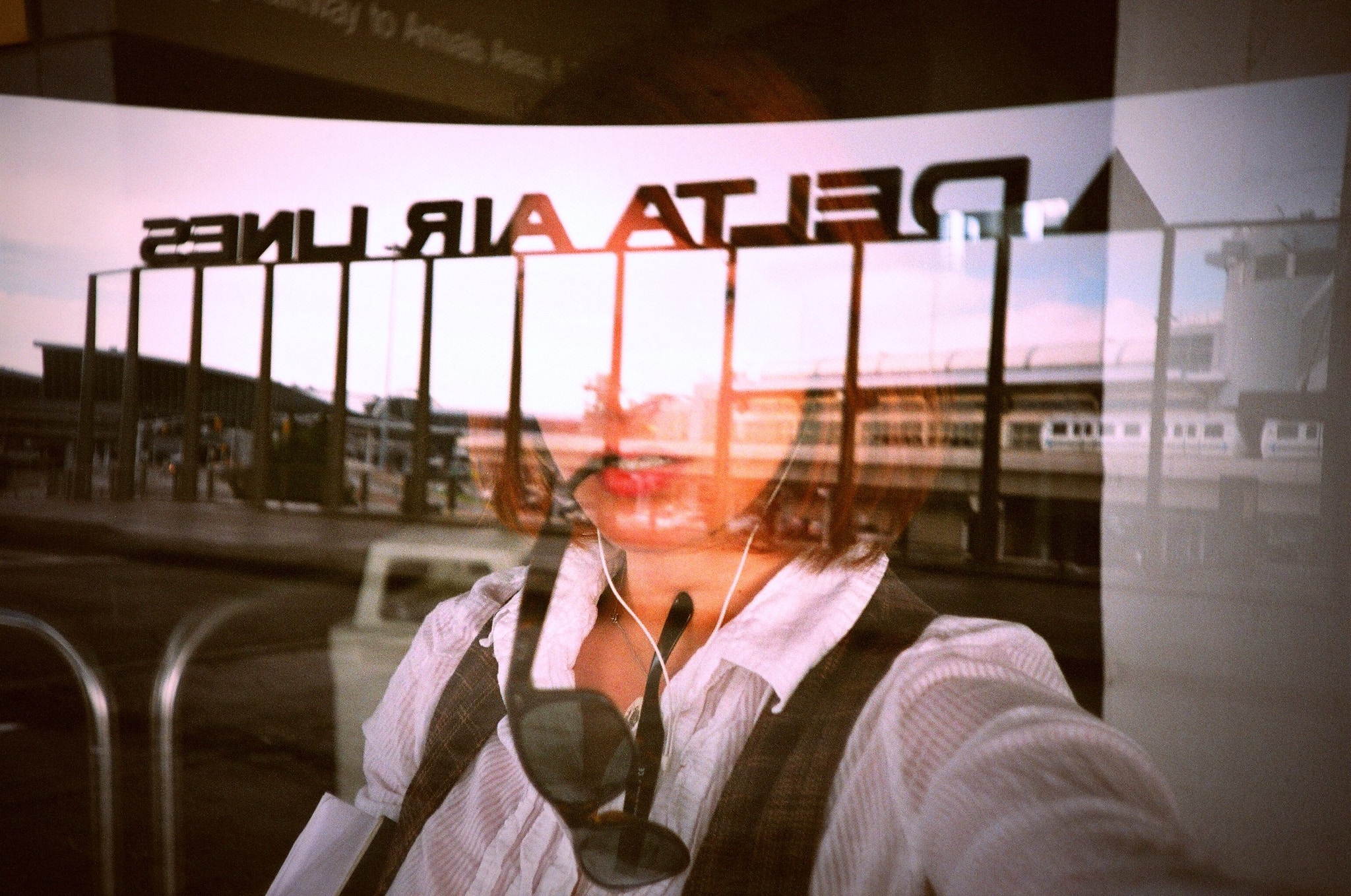 young female traveler looking out the window at an airport, the delta airlines sign visible in the reflection